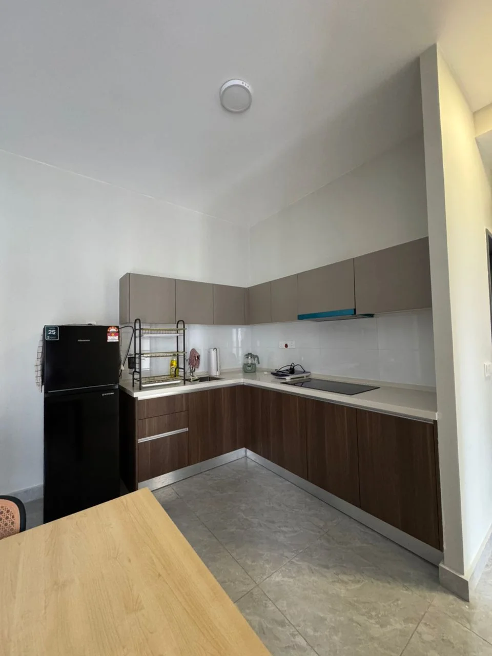 Kitchen features: L-shaped kitchen layout, dark wood cabinetry, light grey upper cabinets, white countertop, stainless-steel sink, built-in stove, black refrigerator, open shelving, grey tile flooring, recessed ceiling lights; style: modern.
